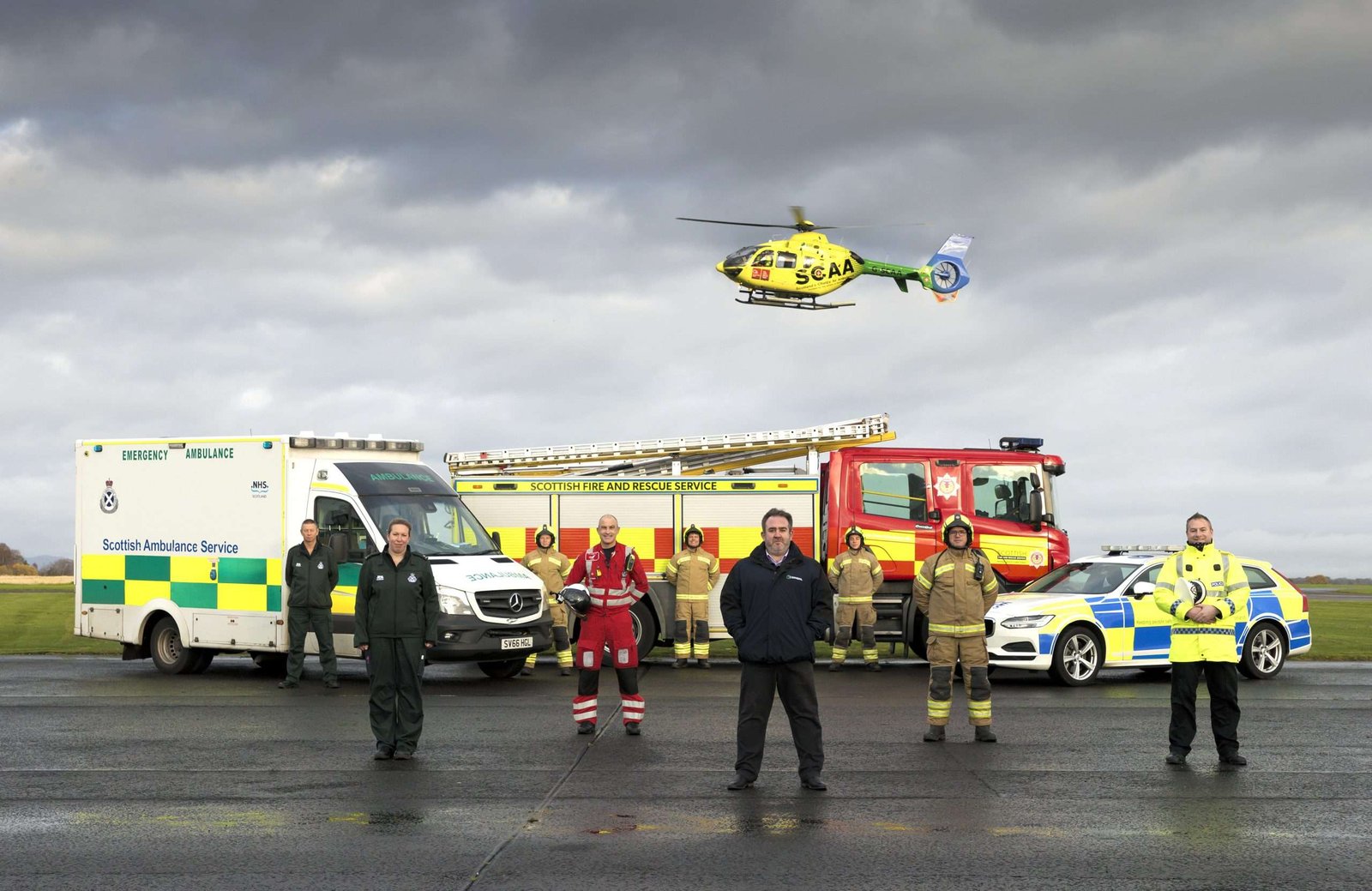 group of adults stood with emergency vehicles in the background